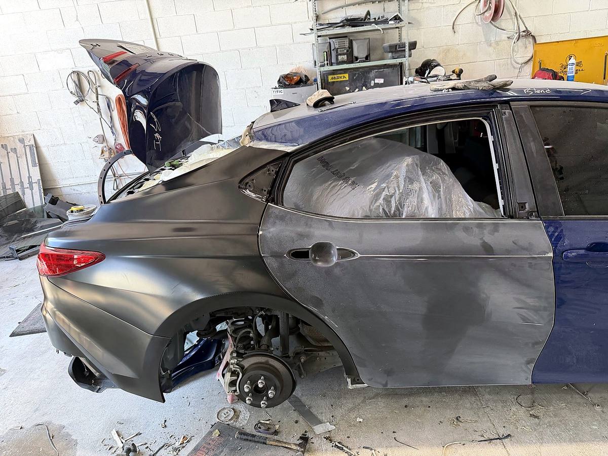 The same sedan with replacement panels fitted and aligned, in primer ready for refinishing