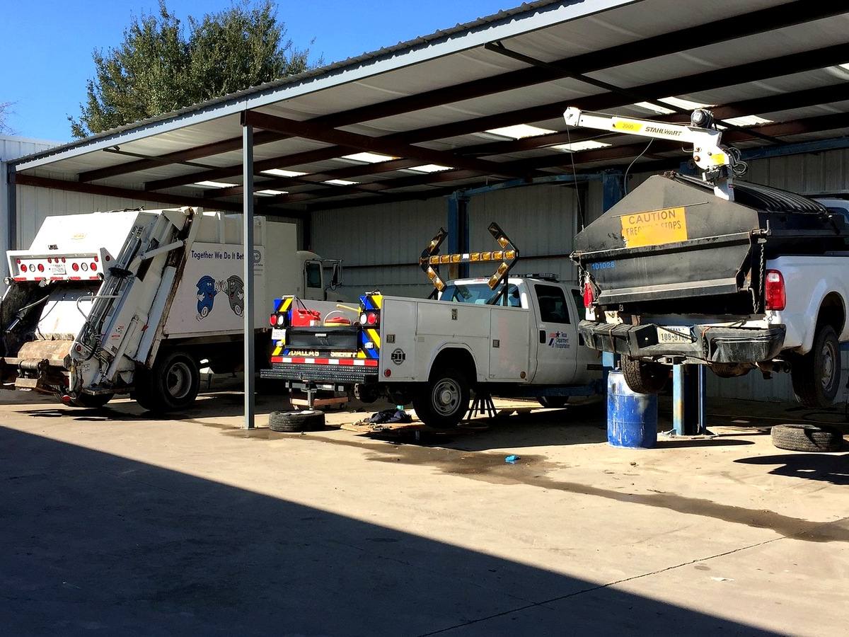 Municipal refuse truck, service-body truck and pickups under repair in the covered work area at First Class Auto