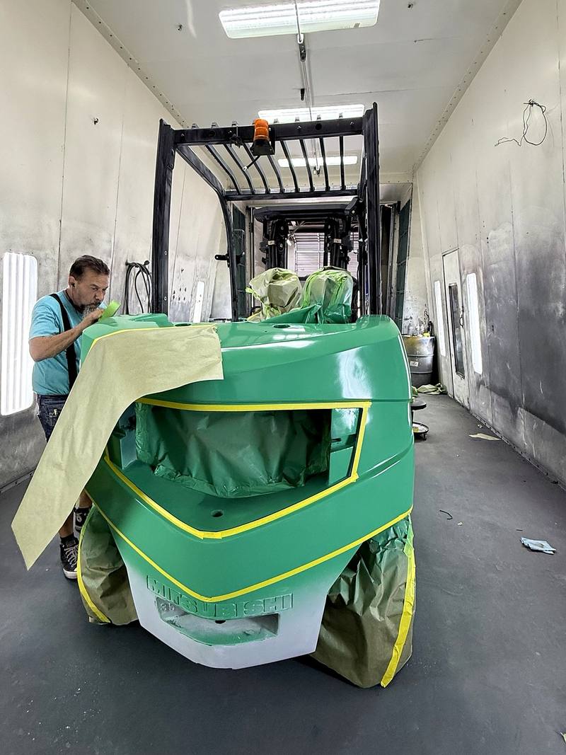 Technician masking the forklift for refinishing inside the paint booth